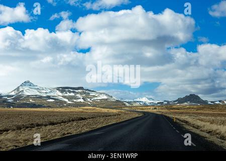 Empty Road Leading Toward Snow Covered Mountains Across Icelandic Wilderness Landscape Stock Photo