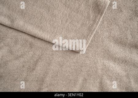 Natural texture of a beige wool fabric. Soft woven cotton texture featuring a draped sleeve from a sweater. Close-up. Top view. Stock Photo
