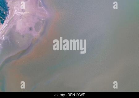 Calm water background texture featuring a pastel pink coastline with natural mineral sediments and immense empty space, perfect for minimalist design concepts in an aerial drone photo. Stock Photo