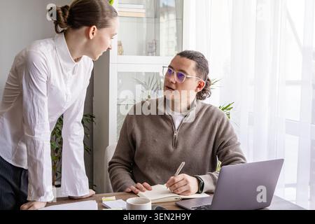 Small multi-generation team working together at table, discussing ideas and taking notes. Focused collaboration, problem solving and productive teamwo Stock Photo