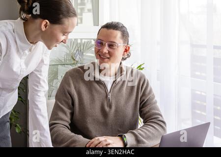 Two coworkers discussing ideas during meeting in bright office space. Modern teamwork, collaboration and communication concept with laptop and natural Stock Photo