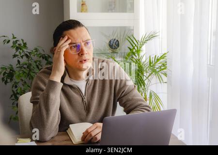Stressed middle aged man touching forehead while sitting with laptop at home desk. Deadline pressure, mental fatigue, burnout and anxiety during remot Stock Photo