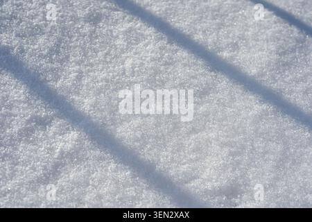 Diagonal Shadow Bands Crossing Fresh Crystalline Snow Surface In Outdoor Winter Scene With Sparkling Granular Texture Under Clear Daylight Creating Soft Tonal Contrast. Stock Photo