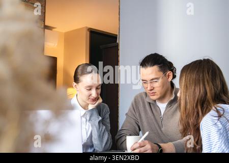 Small multi-generation team working together at table, discussing ideas and taking notes. Focused collaboration, problem solving and productive teamwo Stock Photo