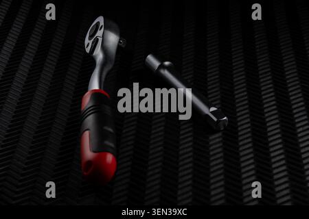 Ratchet wrench and extension bar placed separately on dark textured background. Minimal studio shot showing professional hand tools for mechanical rep Stock Photo