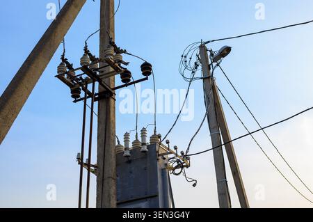 High voltage electrical transformer station is mounted on concrete poles. Ceramic insulators and power grid line wires connect to a utility supply net Stock Photo