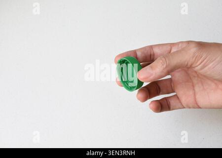 Top view of a human hand holding a green bottle cap isolated on a clean white background. Ideal for packaging, recycling, sustainability, beverage Stock Photo