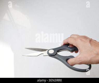 Top view of a human hand holding gray scissors isolated on a clean white background. Ideal for concepts related to office supplies, crafting, cutting Stock Photo