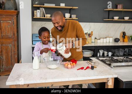 African American father and daughter baking together at marble island using glass bowl and red cups Stock Photo