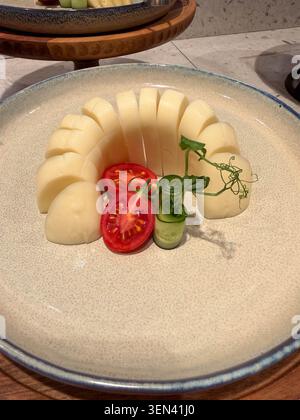 Sliced semi-hard cheese arranged with cherry tomatoes and pea shoots on ceramic plate Stock Photo