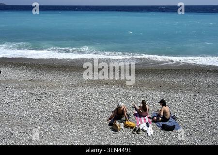 Three women sitting on pebble beach looking out on Mediterranean sea, city of Nice, France Stock Photo