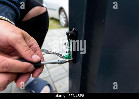 Hand installing an obstacle sensor with network cable wiring on a metal gate post using a screwdriver Stock Photo