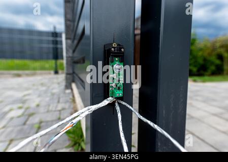 Photocell obstacle sensor installed on a black metal sliding gate panel with exposed network cables Stock Photo