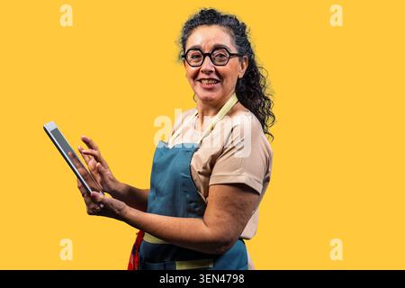 Smiling woman small business owner using a tablet for e-commerce on yellow background Stock Photo
