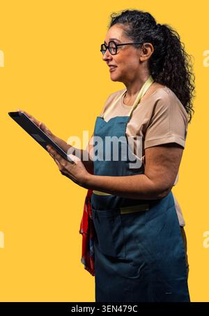 Woman wearing apron and glasses using a tablet, managing her small business Stock Photo