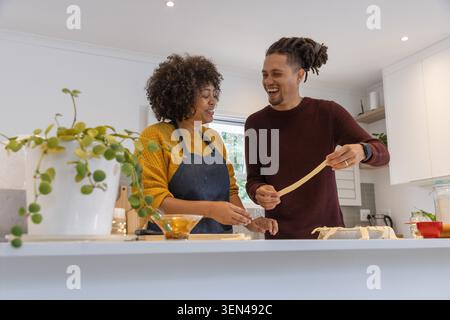 Pasta strips are being stretched and shaped on kitchen island near window, with bowl and plant Stock Photo