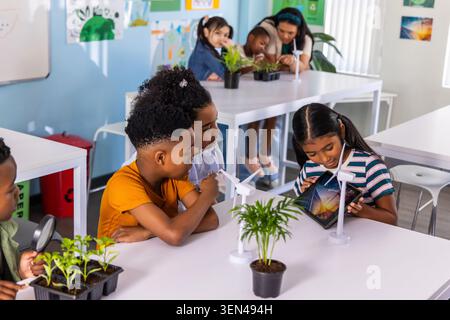 Diverse school children working on wind turbine models and plant using tablet in classroom Stock Photo