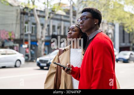 Concentrated african american man and woman tourists wait for taxi while standing on street. Stock Photo