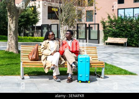 Relaxed african american man and woman travelers on holiday in new city sitting on park bench Stock Photo