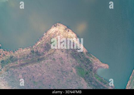 Triangular peninsula land background featuring lush green grass and natural soil textures surrounded by calm river water, perfect for eco travel concepts in a creative top view drone photo. Stock Photo