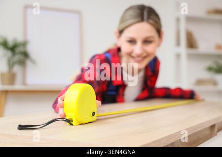 Young woman measuring wooden board with yellow tape measure, home improvement and DIY project Stock Photo