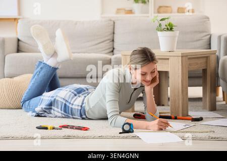 Young woman lying on floor drawing home renovation plans with tools, DIY project and interior design concept, various DIY tools like a tape measure an Stock Photo