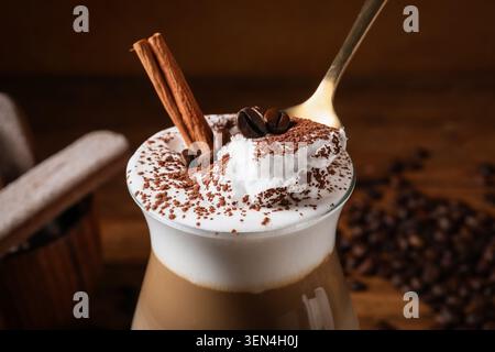 Creamy latte macchiato with whipped cream, cinnamon sticks, coffee beans, and cocoa powder on a wooden table Stock Photo