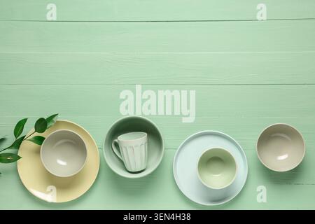 Empty ceramic tableware set with plates, bowls, and mug on light green wooden background for kitchen design Stock Photo