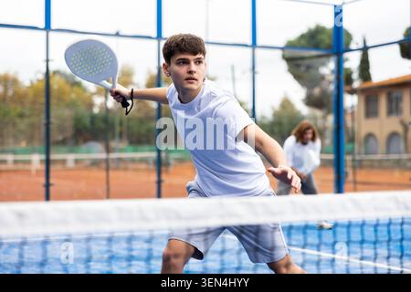 Sportive young man holding padel racquet in hand and ready to return ball while playing in court Stock Photo