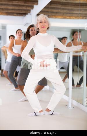 Senior woman and group of adult dancers practice ballet moves in classical dance school. Stock Photo