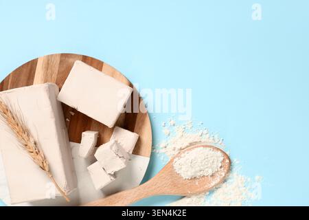 Fresh baking ingredients: compressed yeast blocks, wheat ear, and flour on a wooden board with blue background Stock Photo
