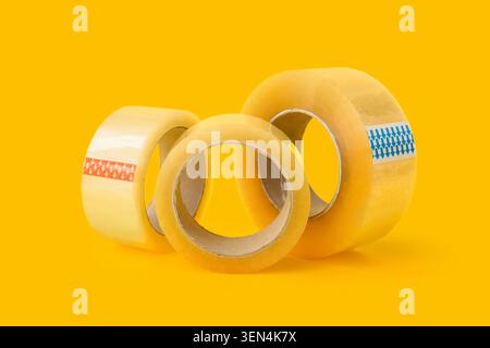 Clear packaging tape rolls with blue and orange arrows on bright yellow background for shipping and office supplies Stock Photo