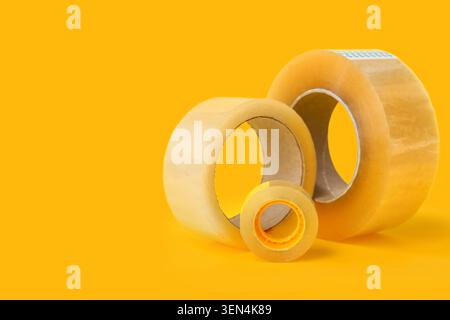 Three clear adhesive tapes of varying sizes for packaging and office supplies on a bright yellow background Stock Photo