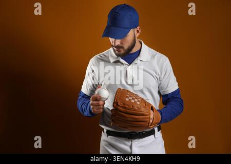 Baseball player in blue cap and white uniform holding ball and glove, sports equipment and athletic gear Stock Photo