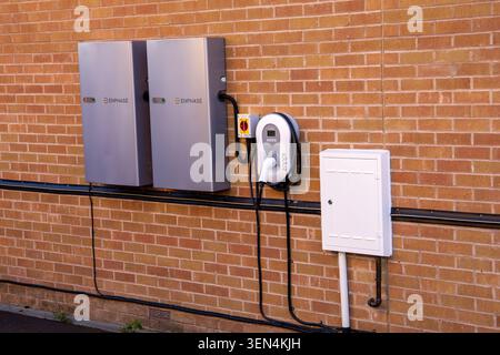 Residential wall-mounted energy storage battery units and an electric vehicle charging station installed on an exterior red brick wall Stock Photo