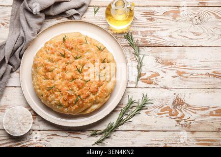 Freshly baked focaccia bread with rosemary and sea salt on rustic wooden table with olive oil and napkin, a small bottle of olive oil and a gray linen Stock Photo