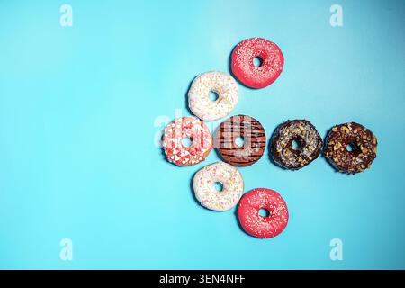 Assorted sweet glazed donuts with sprinkles and chocolate frosting on a bright blue background, delicious dessert variety Stock Photo