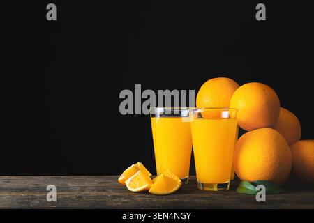 Freshly squeezed orange juice in glasses with whole and sliced oranges on rustic wooden table, whole oranges and orange slices are arranged beside the Stock Photo
