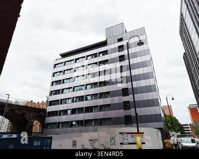 Manchester, UK - May 07, 2026: Contemporary reflective office building in Manchester UK with street scene, construction hoarding and overcast sky. Stock Photo