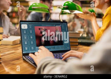 Student uses AI image generator interface on laptop at library study group, showing creative visual results during study session with classmates and green lamps. Text-to-image workflow. Stock Photo
