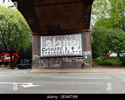 Manchester, UK - May 07, 2026: Billboard poster Choose Life on a brick underpass in Manchester UK with graffiti, trees and an empty street. Stock Photo