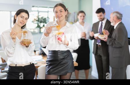 Office workers are eating noodles during their break and chatting with each other Stock Photo
