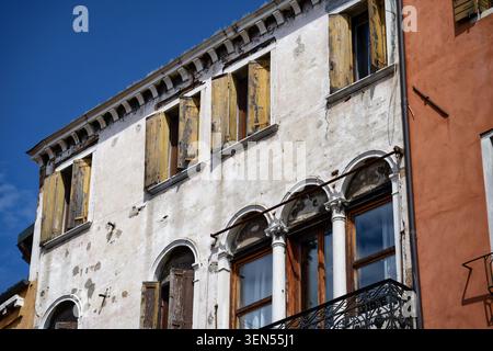 Close-up of a decaying historic house facade in Venice, showing traditional yellow wooden shutters, elegant stone columns, and textured plaster Stock Photo