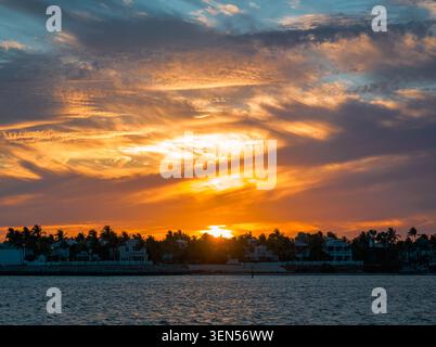 The bright golden rays of the sun break through the dense cloud formations over the dark silhouette of Key West during the summer sunset. Stock Photo