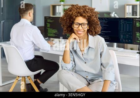 Confident female programmer portrait with code monitors in contemporary office Stock Photo