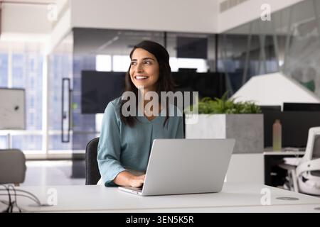 Smiling thoughtful Brazilian woman, office manager working on laptop Stock Photo