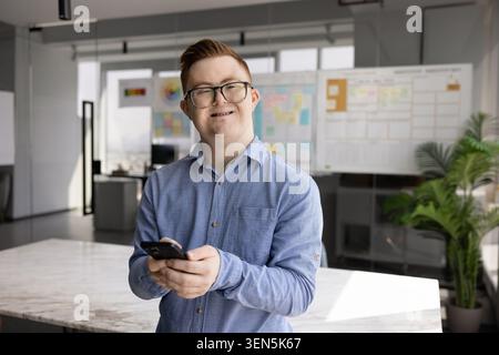 Young man with Down syndrome using smartphone in office Stock Photo