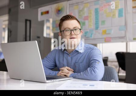 Young man with Down syndrome sitting at desk with laptop Stock Photo