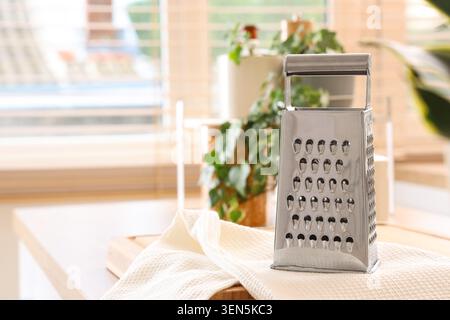 Stainless steel box grater on kitchen countertop with white towel, home cooking and food preparation, the grater features multiple sides with differen Stock Photo