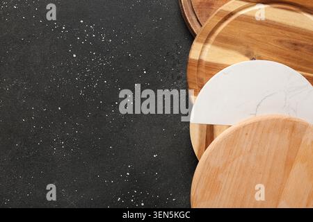 Assorted round wooden and marble cutting boards on dark textured background with copy space, the composition provides ample copy space for design and Stock Photo
